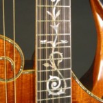 The inlay uses a scroll motif found in many historical harp guitars. The two doves at the 12th fret symbolize peace and music.